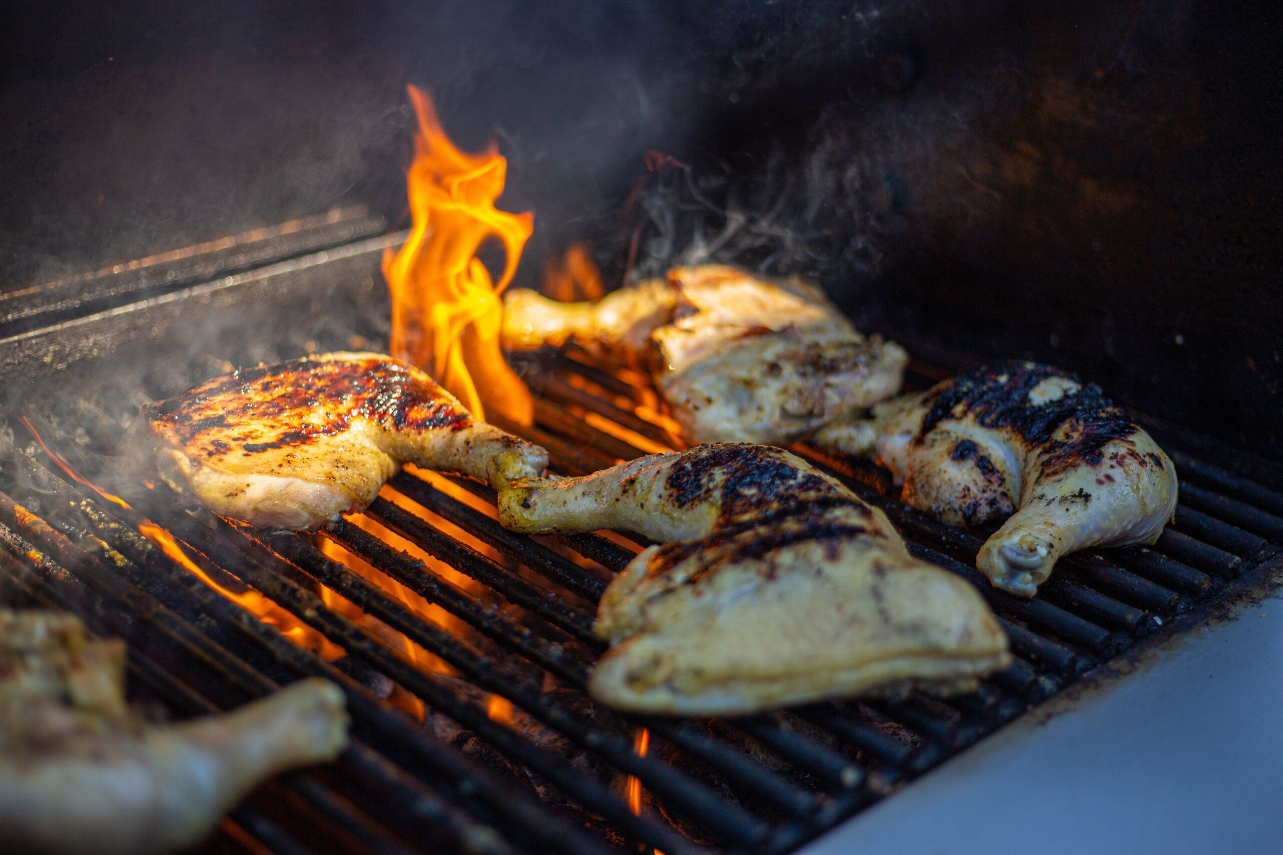 Chicken pieces grilling with flames and smoke rising from the barbecue.