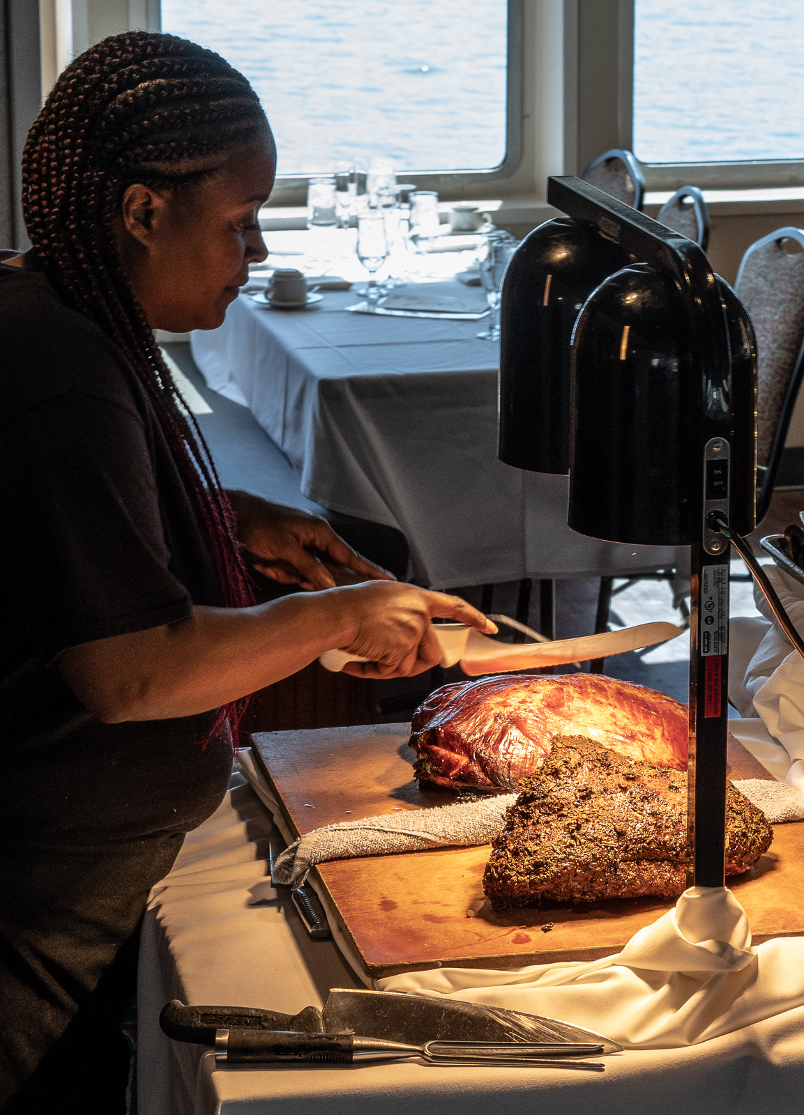 A woman slicing freshly roasted meat at a carving station on a boat, with the open water visible in the background.