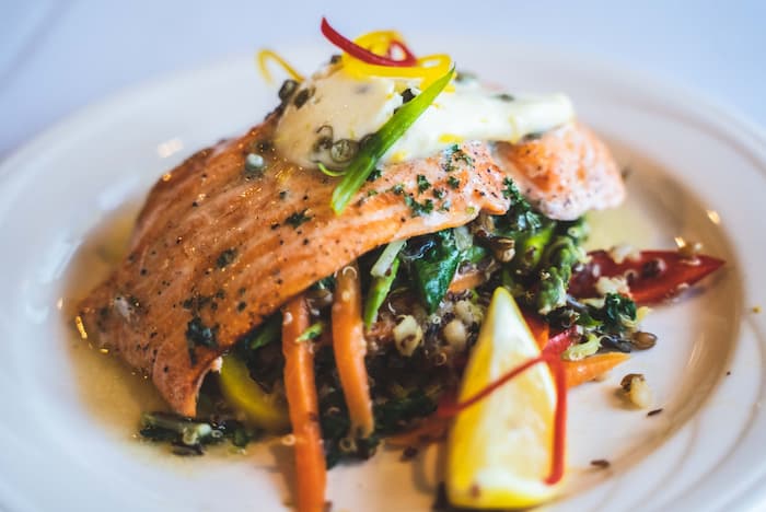 Text: A plate of grilled salmon topped with sauce and garnished with colorful vegetables and quinoa.