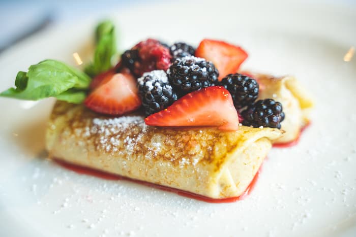 A plate of sweet crepes topped with fresh strawberries, blackberries, and powdered sugar.